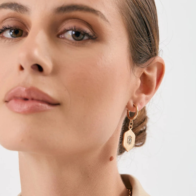 Showcasing the charm crystal drop suspended from a gold mini hoop earring.