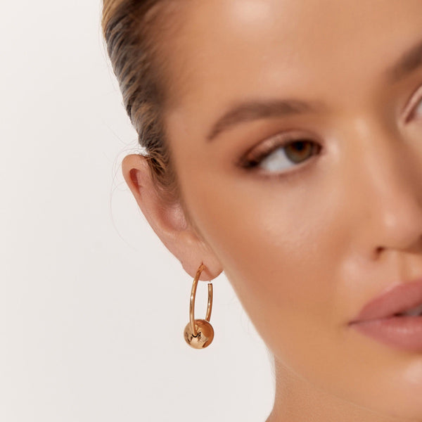 Model inspo image featuring the gold version. These hoop earrings have a metal ball detail and clip in back closure