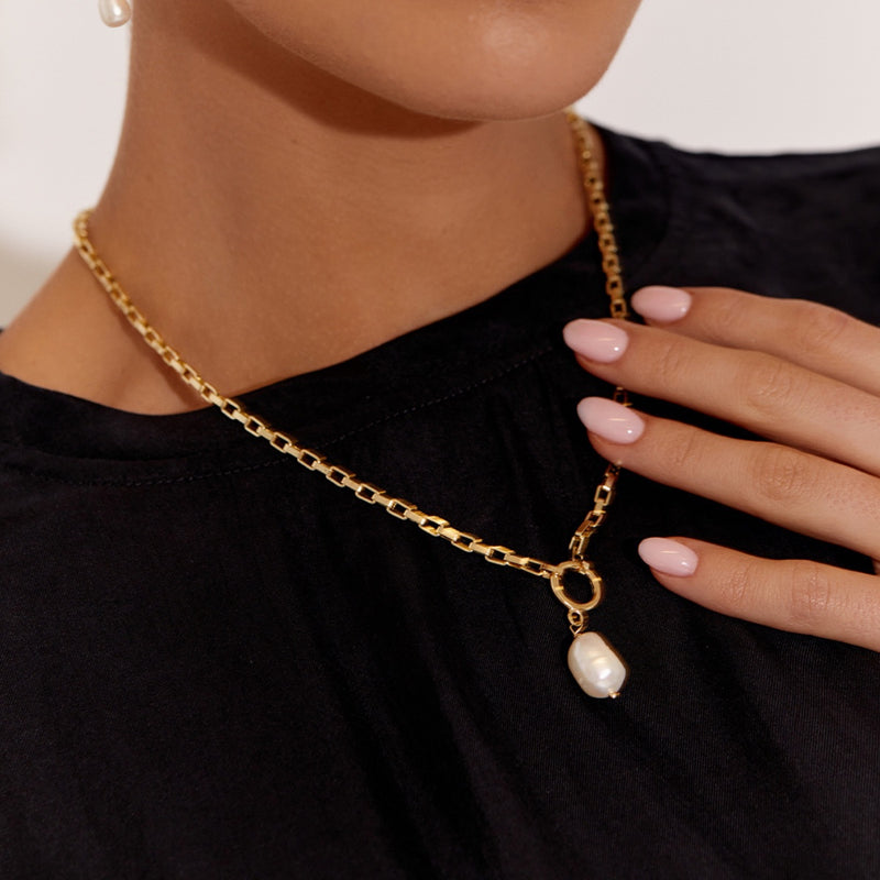 This necklace is being worn by a model in the gold version. A freshwater pearl is suspended from the chain by a circular link