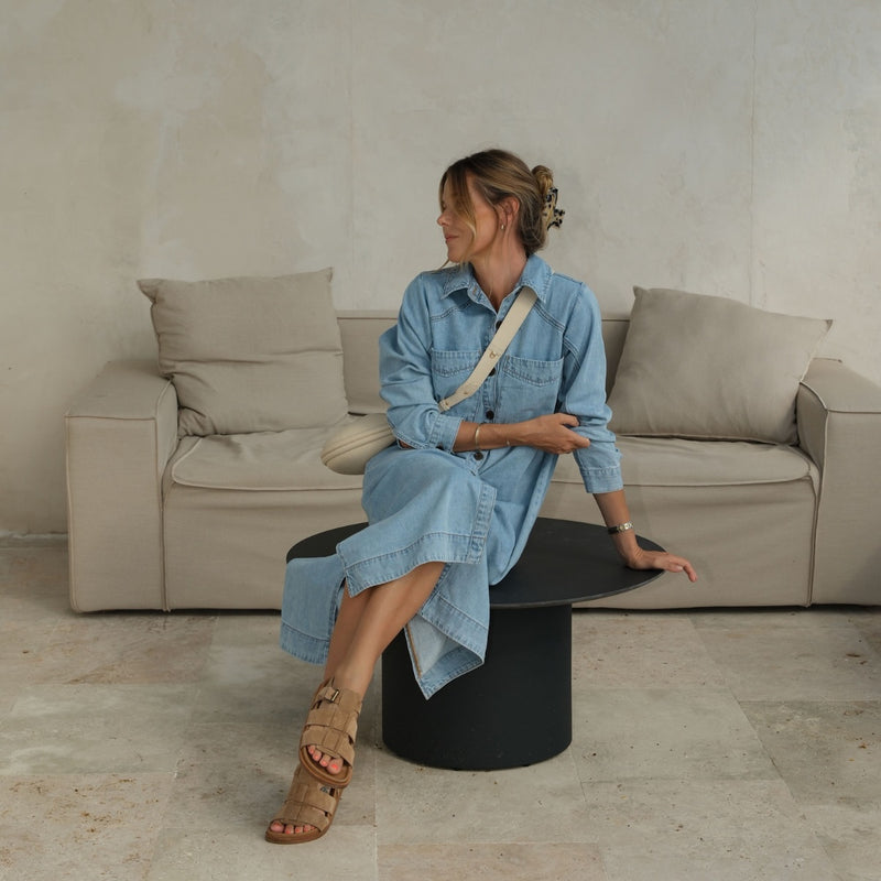 This denim dress has a light blue wash and can be accessorised with a crossbody bag and slides.