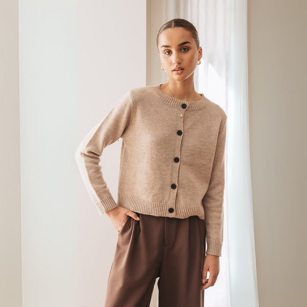 Features a round neckline, black button front and long sleeves.
