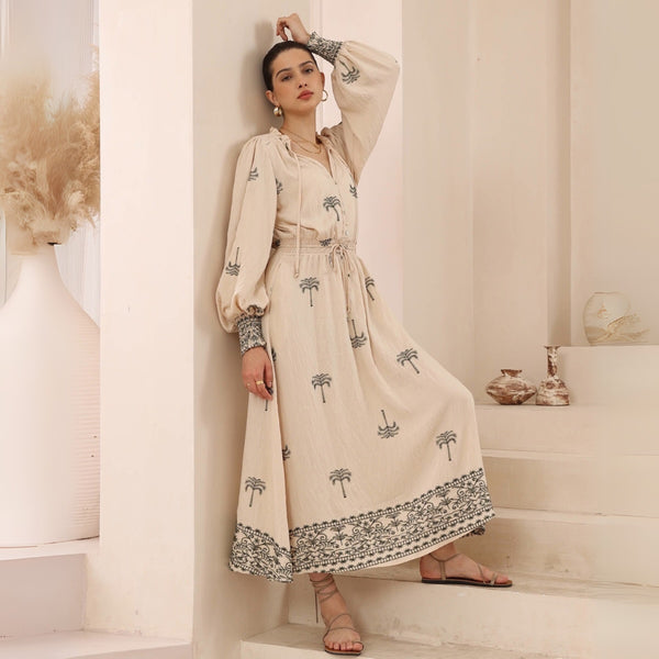 The dress has a shirred waist with drawstring ties, long sleeves and a full maxi length skirt.