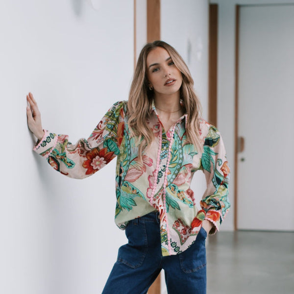 The shirt has a floral and paisley print in muted tones of pink, green and red.