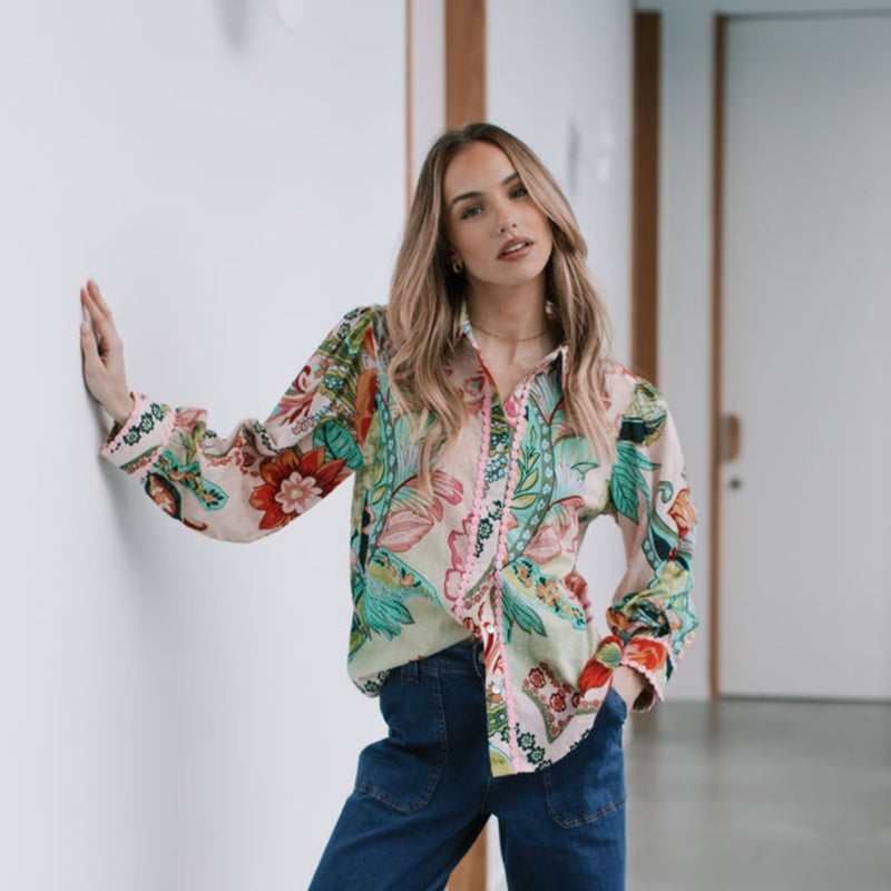 The shirt has a floral and paisley print in muted tones of pink, green and red.