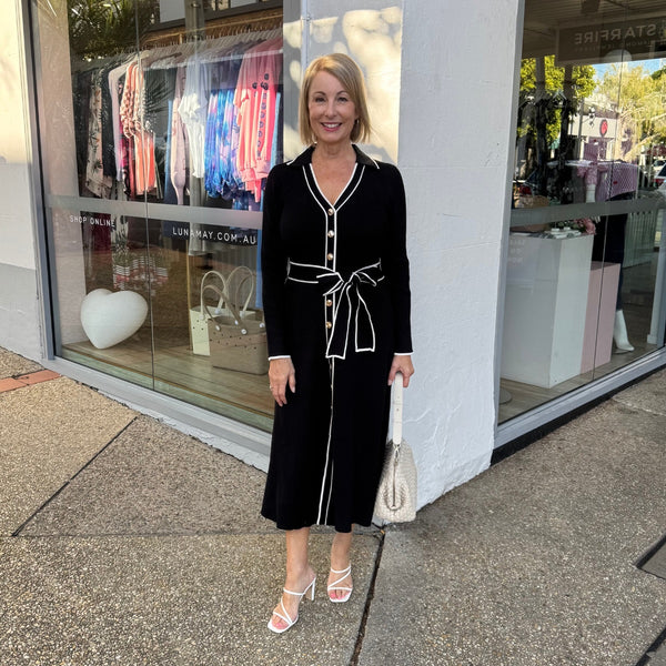 This black midi dress features a collar, V neckline, gold buttons down the front, long sleeves and it has an Aline skirt.