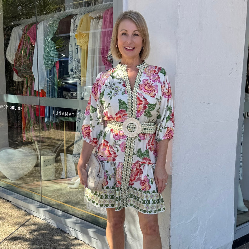 The dress has a mock collar, button front, detachable belt with raffia buckle, half length sleeves and it finishes above the knee.