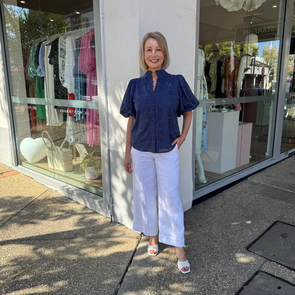 This top is made from a broderie lace fabric in navy and features a mock collar, button front, short puff sleeves.