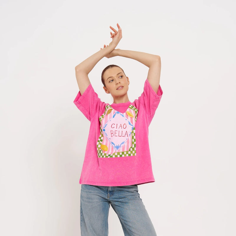 Maku Ciao Bella Tee with an acid wash pink base and a colourful Ciao Bella print on the front in white, blue, green and it also has lemon illustrations.