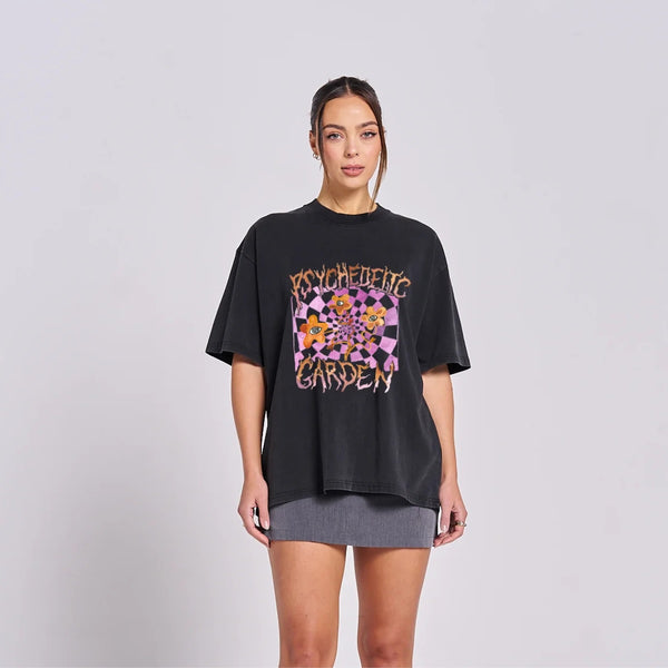 Maku The Label Psychedelic Garden Tee in a washed black base. It has a colourful floral print on the front in lilac and orange. Features a round neckline, drop shoulder and its longer length.