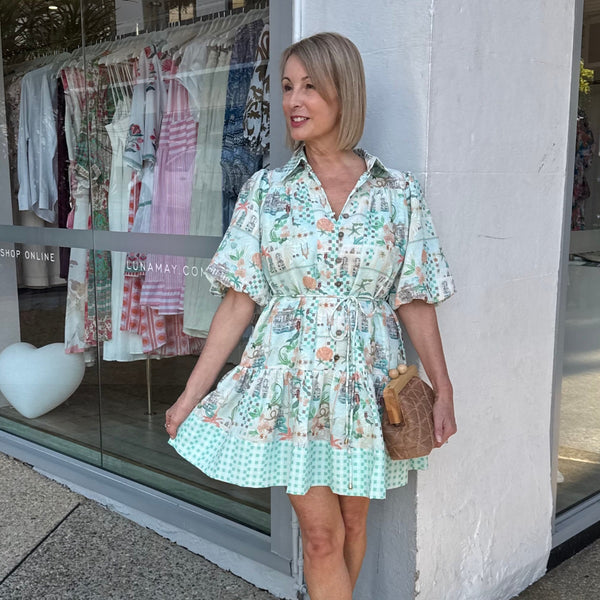The dress features a collar, short sleeves, narrow self fabric waist tie and a tiered mini skirt.
