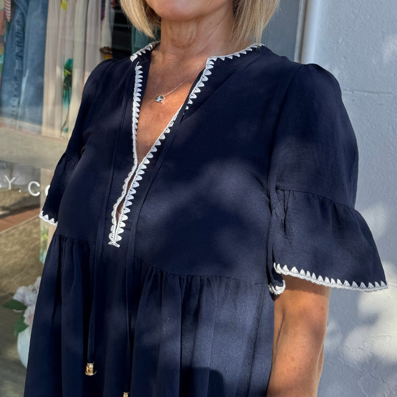 Close up of the bodice area including neck ties finished with a gold bead and the white stitch detailing extending along the neckline and sleeve edge.