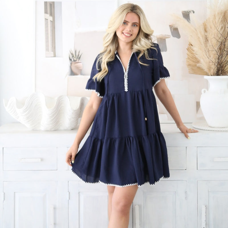 Our Renee Dress is available in navy. This short dress has a V neckline with ties, short sleeves with frill edge and a tiered body.