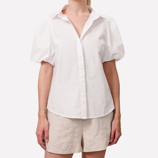 The Alice Shirt has a collar, short puff sleeves, button front with a hidden placket and this white cotton top has a curved hemline.