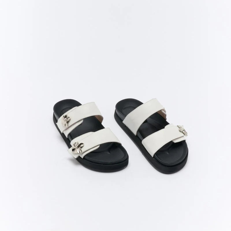 These slides have two upper straps in an off-white colour with a silver metal butterfly accent.